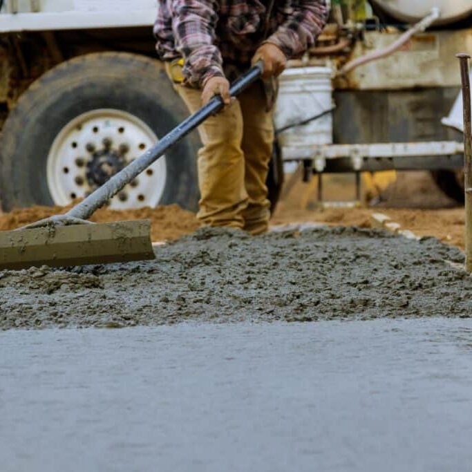Construction worker pour cement for sidewalk in concrete works with mixer truck with wheelbarrow at construction site filling formwork with cement and gravel
