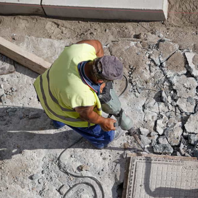 Construction worker with jackhammer drilling concrete on sidewalk. City Maintenance concept